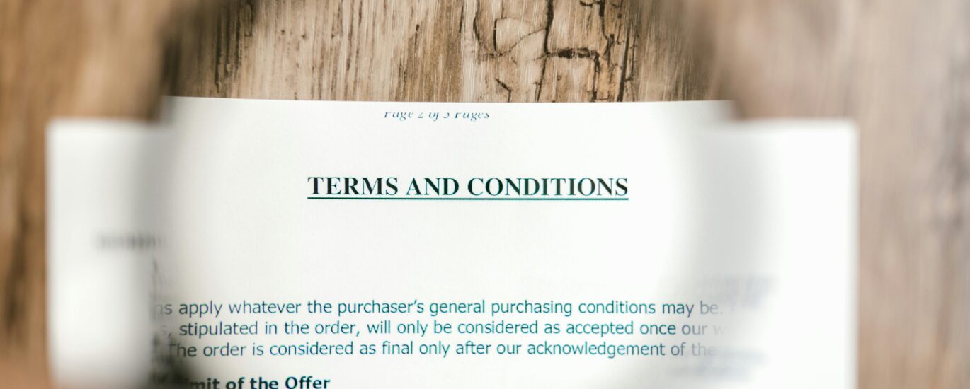 Magnifying glass focusing on terms and conditions document on wooden surface.